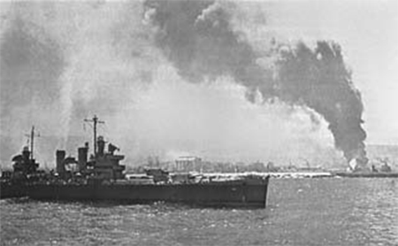 En primer plano, el Crucero USS Savannah. En el fondo, efectos del bombardeo