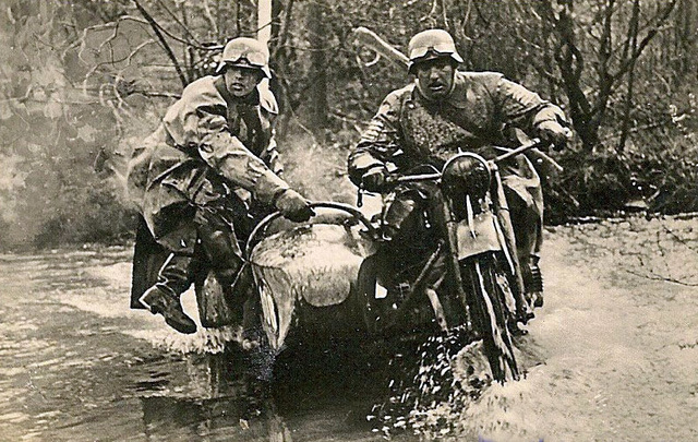 Un equipo de reconocimiento en su motocicleta trabajando juntos para mantener el equilibrio mientras cruzan un arroyo