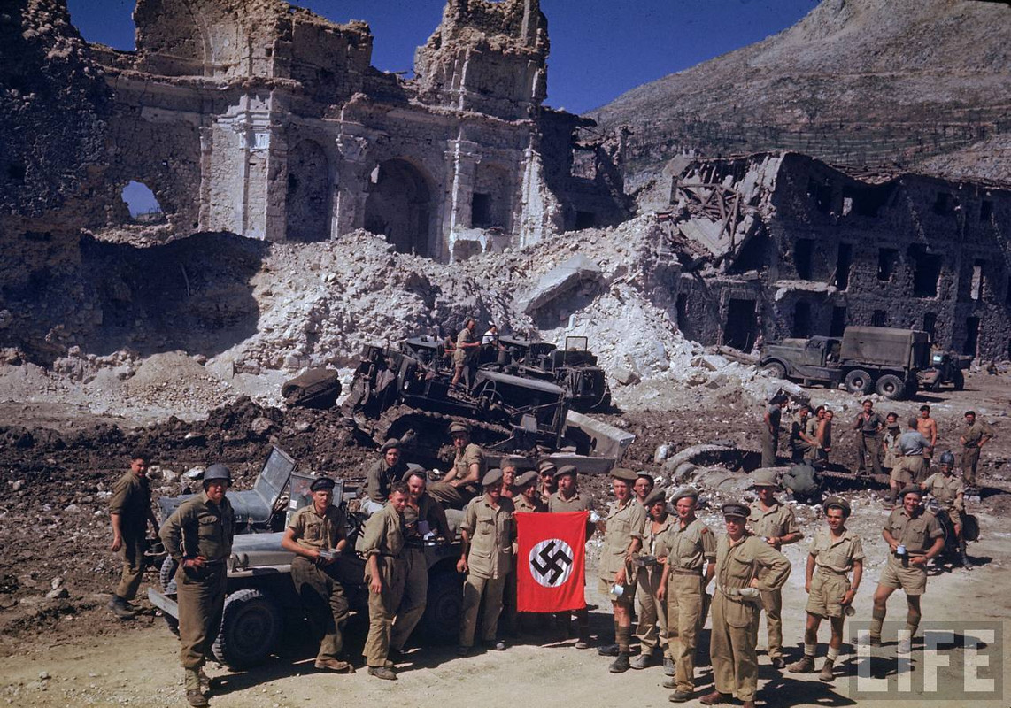 Soldados británicos y sudafricanos levantan una bandera alemana usada como trofeo, mientras que los ingenieros intentan abrirse paso a través de los escombros