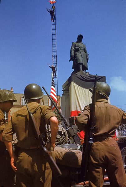 Soldados americanos observan a los habitantes de Avranches izar las banderas francesa y americana en la principal plaza del pueblo