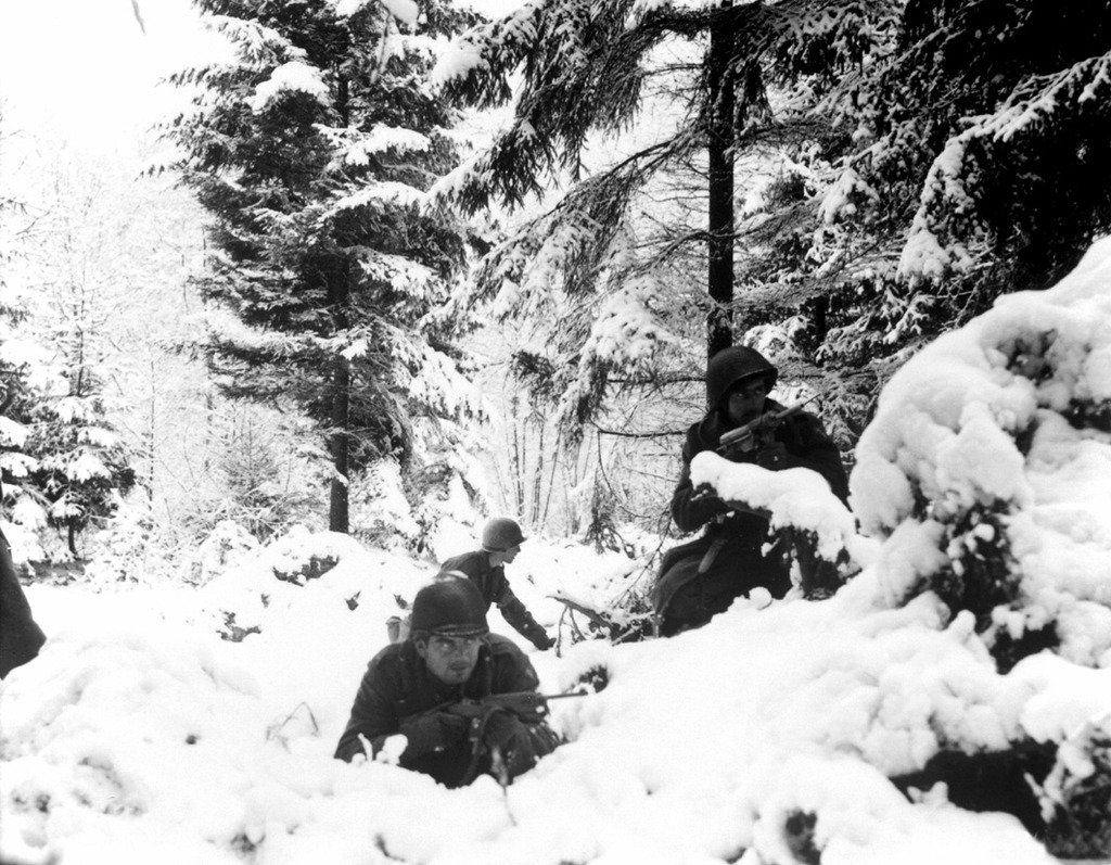 Infantería americana se cubre en la nieve en Bastogne,portan una carabina M1 y un subfusil M3 Grease Gun