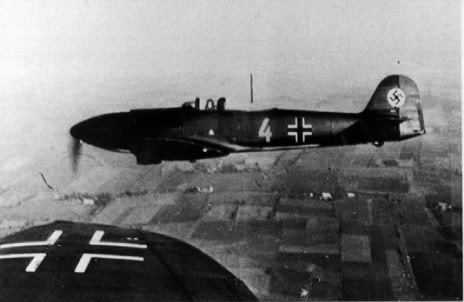 El Amarillo 4, código de fábrica HE+JA, vuela en formación con otra aeronave del IV. JG132. La Balkenkreuz, cruz de barras, del ala de avión en primer plano estaba hecha con rectángulos blancos contra el color de camuflaje, mientras que la del Amarillo 4 eran más estrechas y tenía la usual cruz negra. Una esvástica negra en el centro de un círculo blanco, aplicada sobre una franja roja, eran las marcas típicas usadas por los aviones de la Luftwaffe hasta el 1 de enero de 1939. Justo debajo de la Hakenkreuz, esvástica, se encontraba el número de construcción, Werknummer, en blanco