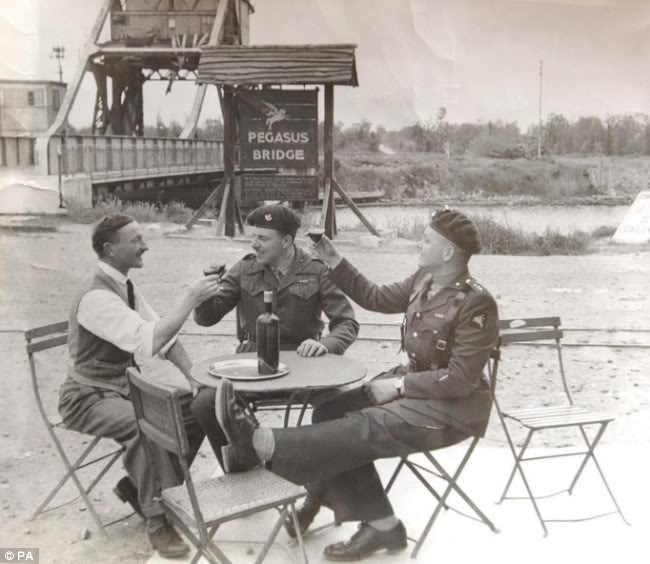 El Capitán Wood, el Mayor John Howard, centro, y Georges Gondrée, izquierda, brindan en una mesa al lado del puente en 1946