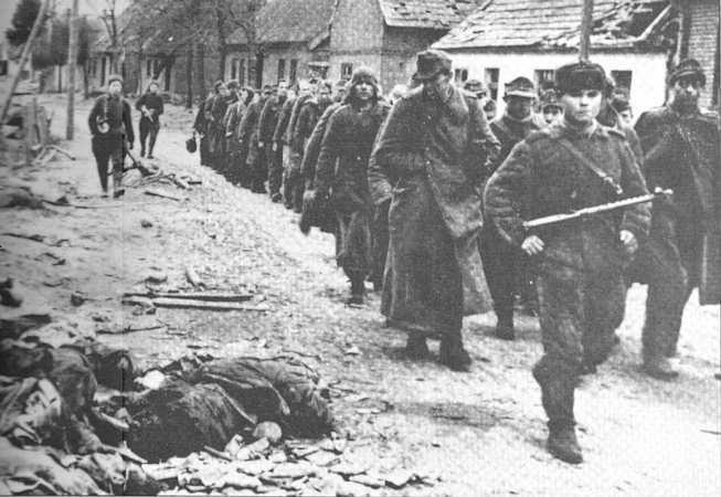 Columna de prisioneros alemanes custodiados por elementos del Ejército Rojo pasan por delante de un soldado alemán muerto en combate