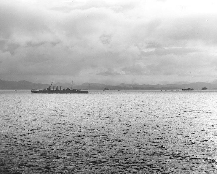 El Crucero Australiano HMAS Canberra, al centro a la izquierda, protege tres buques de transporte aliado, al fondo y al centro a la derecha, que descargan suministros y desembarcan tropas en Tulagi