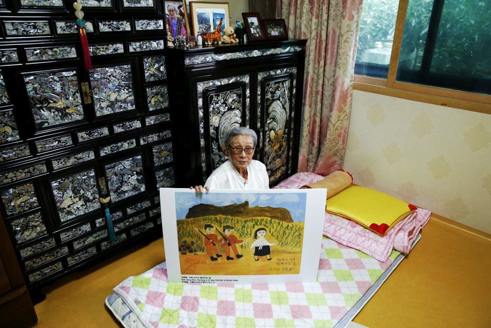 Kim Bok-dong, antigua mujer de solaz surcoreana, posa con una copia de su pintura titulada El día que una niña de 14 años es raptada en su habitación del refugio La casa compartida para mujeres víctimas de los abusos sexuales de las tropas japonesas durante la Segunda Guerra Mundial. Durante una sesión de dibujo terapéutico con el que en la residencia intentan aliviar el trauma que ha quedado a estas mujeres, Kim realizó esta obra para describir lo que le ocurrió a ella. En 1940 fue secuestrada por tropas japoneses y usada como esclava sexual unas 15 veces al día entre semana y hasta 50 los sábados y domingos en varios burdeles militares en China, Hong Kong, Sumatra, Java, Malasia y SIngapur hasta que Japón se rindió
