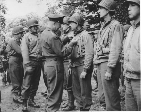 El general Eisenhower impone medallas a varios oficiales con un sonriente general Bradley a su lado durante la campaña de Normandía. Todos los militares de la fila llevan chaquetas de combate de invierno, incluido Bradley, quien era un apasionado de esta prenda, como demuestra el archivo fotográfico del conflicto