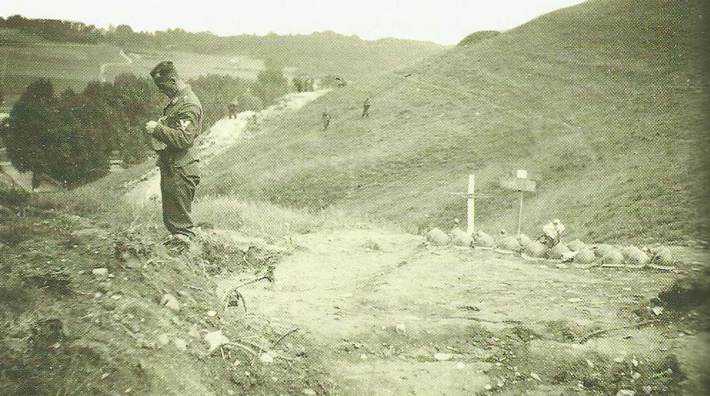Un paracaidista alemán en la Colina de Kanne, junto a una fosa común de caídos belgas