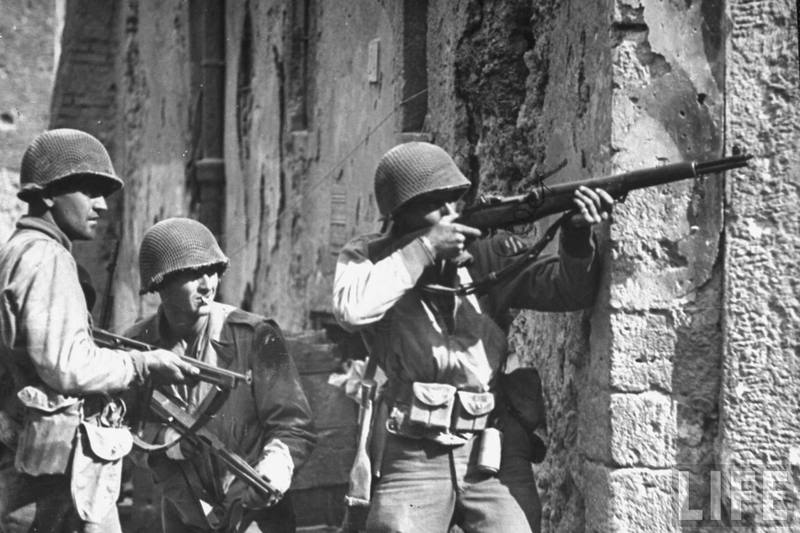 Soldados estadounidenses combatiendo en alguna ciudad de Europa Los dos de la Izquierda llevan subfusiles Thompson M1A1, mientras que el restante un semiautomático M1 Garand